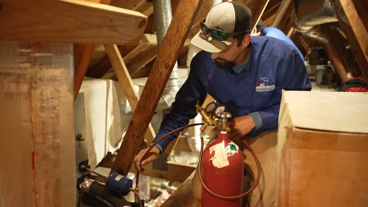HVAC technician servicing attic AC unit in San Antonio